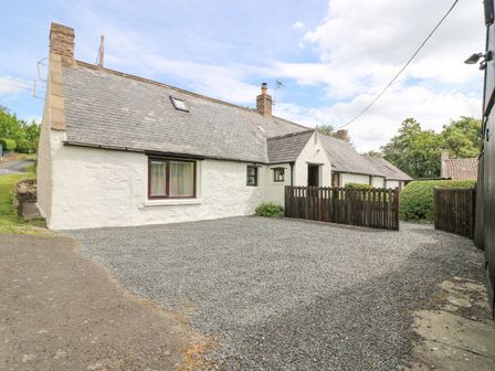 A white stone house with a slate roof and gravel driveway with wooden gate at Loanview in Cornhill-On-Tweed