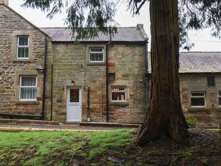 The exterior of a stone building with windows a white door and a large tree in the foreground at Gardeners Rest in Loftus near Easington