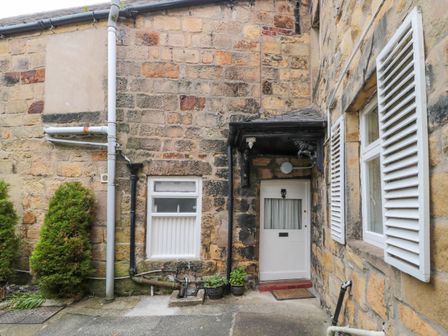 Exterior view of a stone building with a white door and windows with shutters at White Swan Cottage in Alnwick