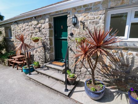 Stone exterior wall with green door steps potted plants and a wooden bench at Chy-An-Oula in Seworgan near Constantine
