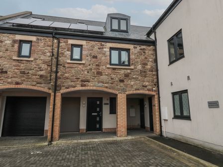 A parking area in front of a building with stone and brick facade and black doors at Greenlee House in Seahouses