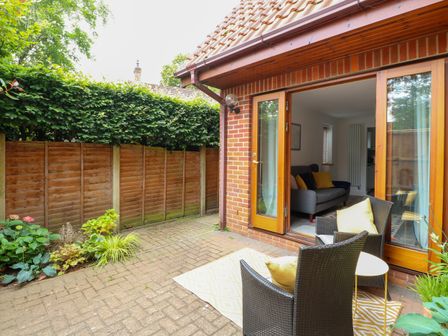 A small patio area with two chairs and a table outside a room with open wooden double doors at The Annexe at Number 4 in Coltishall