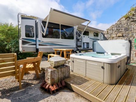 An outdoor seating area with wooden benches and table next to a hot tub and a large camper van at Tickeydoo Tor Down Quarry in St Breward