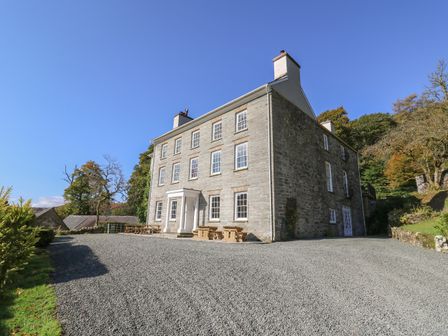 A large stone building with multiple windows and chimneys surrounded by gravel and trees at Llwynderw Hall in Abergwesyn near Llanwrtyd Wells