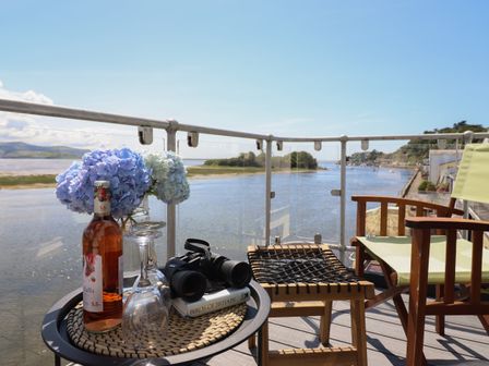 A balcony with a bottle of wine glasses binoculars and flowers overlooking a river at Estuary Escape in Porthmadog