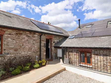 An exterior view of a stone building with solar panels on the roof and a small garden bed at Woodland Roost in Parkham near Bideford