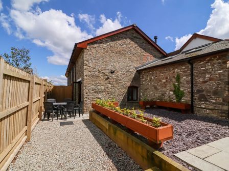 An outdoor patio with a stone building wooden fence black chairs and table and raised planters at Ladybird Rest in Parkham near Bideford