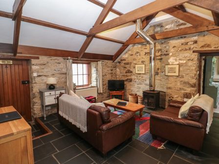 A living room with two leather sofas a wooden coffee table a wood burning stove and stone walls at Preseli Hills Cottage in Pontfaen near Fishguard