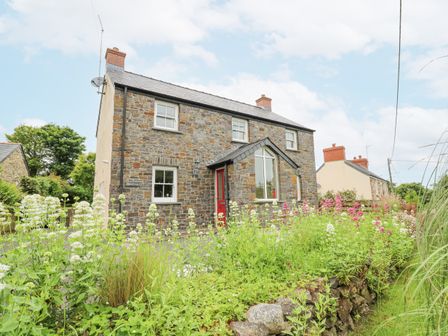 A stone house with a red door and flowering plants in front at Beachway in Brynhenllan near Dinas Cross