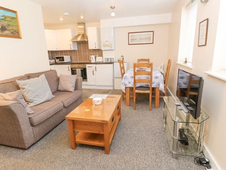 An open living room and kitchen with a sofa coffee table dining table and chairs and a television on a glass stand at Greenwood Apartment in Carbis Bay