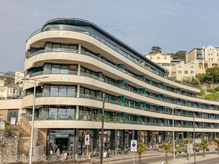 A multi-story building with glass balconies and shops on the ground floor at Apartment 17 Abbey Sands in Torquay