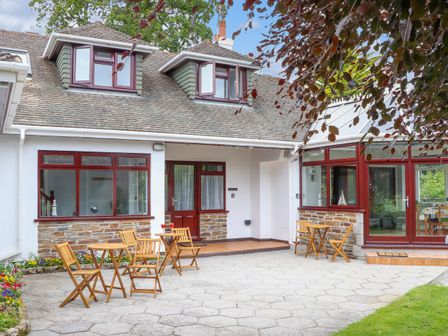 A house exterior with wooden chairs and tables on a paved patio at Squirrels Leap in Falmouth