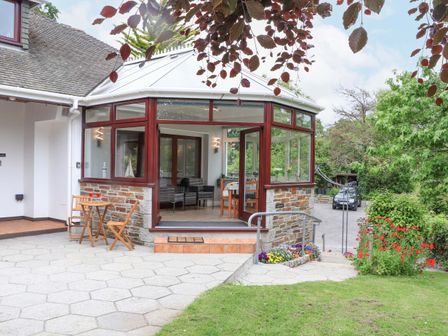 An outdoor patio area with a small wooden table and two chairs next to a conservatory with glass windows at Lake View in Swanpool Nr Falmouth