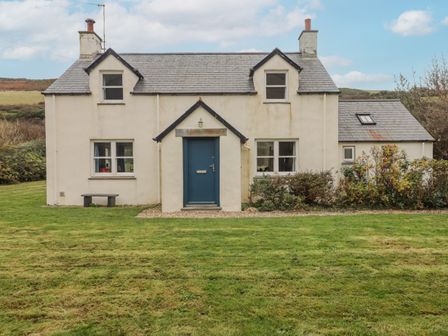 A two-story house with a blue door and grass lawn at Ger Y Traeth in Pwllgwaelod near Dinas Cross
