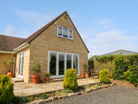 An exterior view of a house with stone walls and sliding glass doors surrounded by potted plants and bushes at Monument View in Hawkesbury Upton