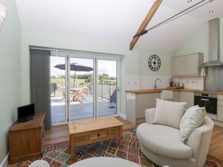 A living area with a round sofa and wooden coffee table next to a kitchen with wooden countertops and cabinets at Singletree Cottage in Swainsford near Mere