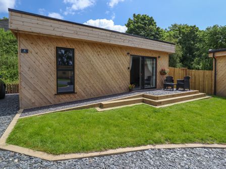 An outdoor patio area with two black chairs and a table beside a wooden lodge with sliding glass doors at Valley Lodge 4 - North Wales Eco Lodges in Graigfechan near Ruthin