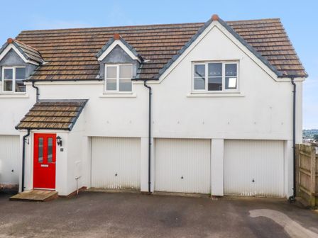 A white house with a red door and three garage doors under a tiled roof at 20 Keay Heights in St Austell