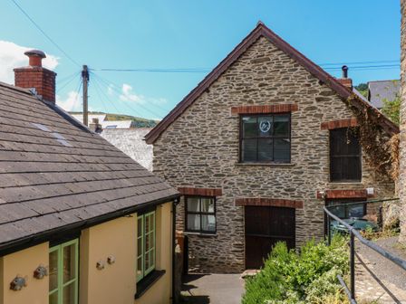 A stone building with windows and doors next to a yellow house with green windows at The Old Smithy in Lynton