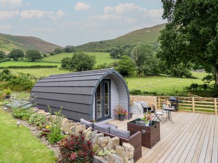 A cabin with a deck and furniture near a green landscape at Caban Tirion in Dinas Mawddwy near Dolgellau