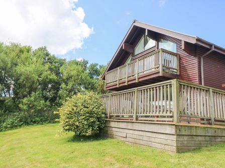 A wooden house with two balconies and a green lawn with bushes at The Willows in Winnard's Perch near St Columb Major
