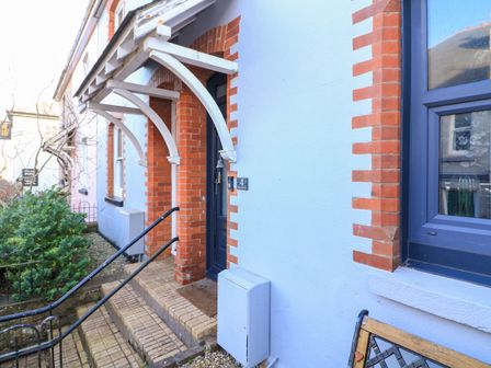 The front entrance of a house with a small overhanging roof supported by white beams and steps leading up to a dark door at 4 Alma Terrace in Malborough