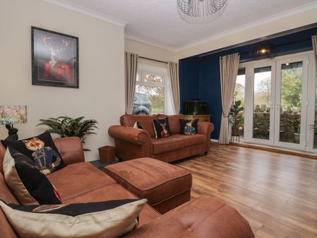 A living room with brown sofas and animal print cushions near windows and glass doors at Benstead Cottage in Gosforth