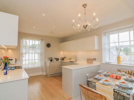 A kitchen with white cabinets a dining table set with plates and croissants and two windows with blinds at 4 The Manor House Hillfield Village Dartmouth
