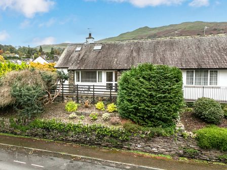 A stone and slate roof house with bushes and a stone retaining wall at Lyndhurst in Ambleside