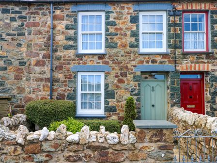 A stone cottage exterior with green and red doors and white windows at Orielton Cottage in Dinas Cross
