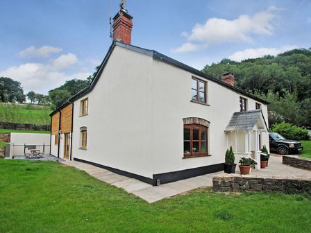 Exterior view of a white two-story house with wooden windows and doors on a grassy lawn at Exmoor Farmhouse in Bampton Devon
