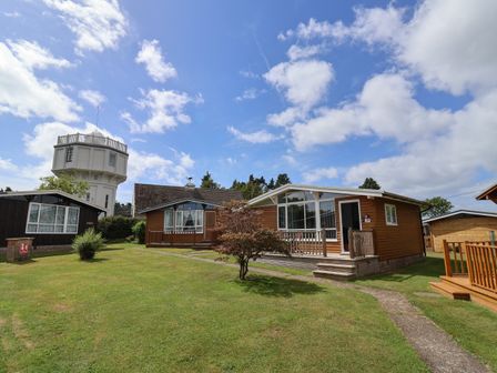 Wooden chalets on a grass lawn with a tall white water tower and blue sky at Pebble Beach Chalet in Seaton