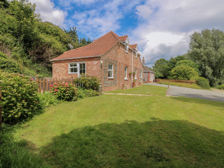 A brick house with a red tiled roof surrounded by grass and trees at Dairy Cottage West Caister near Caister on Sea