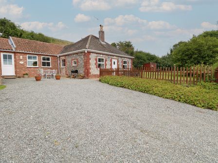 A gravel driveway leading to a brick and flint house with a patio set and wooden fence at Flint Cottage in West Caister near Caister-on-Sea