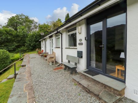 A row of white cottages with gravel path benches and patio furniture surrounded by greenery at Bluebells Chapel Stile