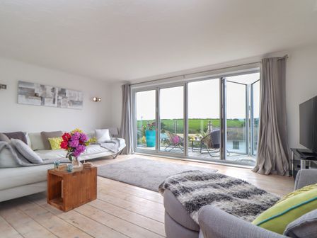 A living room with sofas a wooden coffee table and glass doors opening to a balcony at Tidal View in Newquay