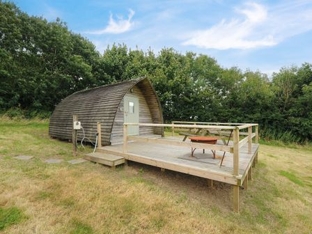 A wooden pod structure with a deck table and fire pit on a raised wooden platform at Sheep Shed Penbugle Organic Farm in St Keyne near Looe