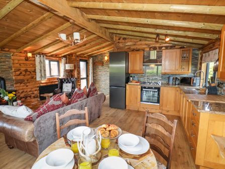 A kitchen and dining area with wooden cabinets a table set with plates and glasses and a living area with sofas and armchair at Stag Lodge Holiday Retreat in Whitby