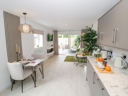 A kitchen and dining area with a small table set for two and a living area with a green sofa and sliding doors at The Croft in Shipston-On-Stour