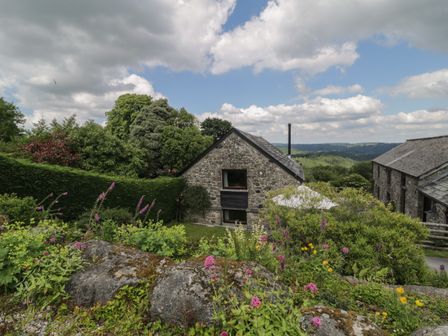A garden with flowers rocks and bushes in front of stone cottages with a view of hills at Beckaford Cottage in Bovey Tracey