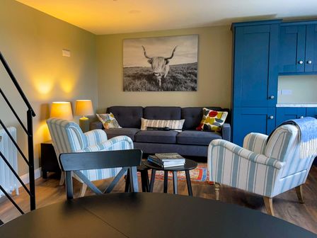 A living room with a gray sofa pillows striped armchairs side tables and blue cabinets at Narrow Gauge Cottage in Armoy County Antrim