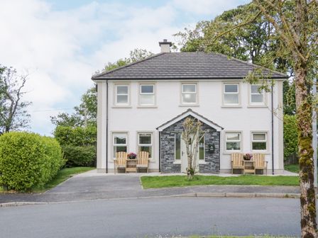 A two-story house with white walls and grey roof with outdoor wooden chairs and a small stone porch at Stoneywood in Culdaff County Donegal