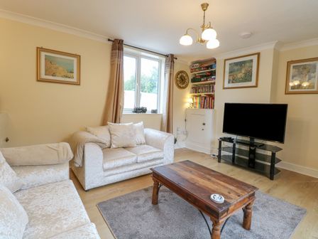 A living room with two sofas a wooden coffee table a television on a stand and framed pictures on the walls at Tiffany's Cottage in Gorleston-On-Sea