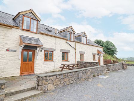 Stone cottage with wooden doors and windows picnic tables outside and stone wall at Llys-y-Wennol in Penmachno