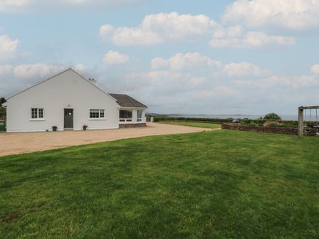 A white house with green door and windows surrounded by green grass and a gravel driveway at Cois Leice in Cushlecka near Mulranny County Mayo