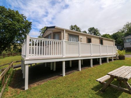 A mobile home with white railings on a raised platform surrounded by grass and trees at 23 Manleigh Park in Combe Martin