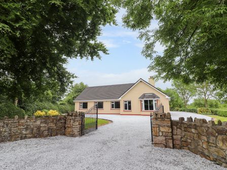 A single story house with a gravel driveway and a stone gate surrounded by trees at Fort Lodge