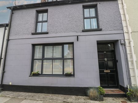 A grey two-story house with black window frames and door with plants on the sidewalk at Bryn Siriol in Narberth