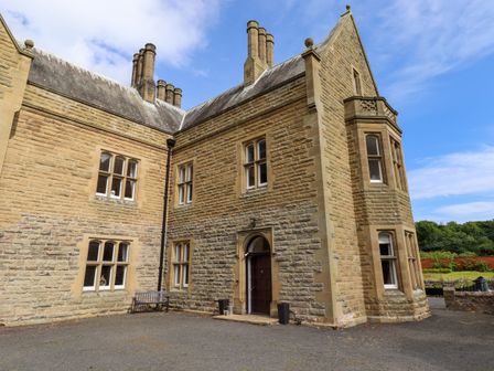 An exterior view of a stone building with multiple chimneys and windows at North Wing Middleton Hall Estate near Belford