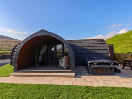 An arched cabin with a chair and potted plants next to a hot tub and picnic table at Oyster Catcher in Chapel Le Dale near Ingleton